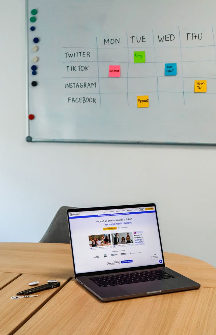 Un espace de bureau contemporain mettant en scène un ordinateur portable et un planning sur tableau blanc destiné aux plateformes de réseaux sociaux.